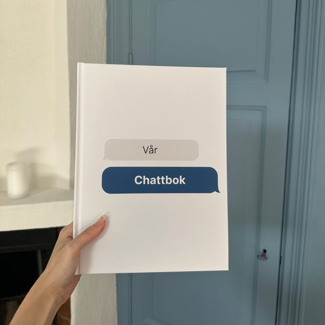 Vit hårdpärmsbok med texten ’Vår Chattbok’ på omslaget, inspirerad av chattbubblor – en personlig bok skapad av meddelanden.