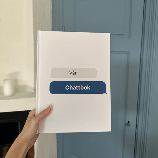 Vit hårdpärmsbok med texten ’Vår Chattbok’ på omslaget, inspirerad av chattbubblor – en personlig bok skapad av meddelanden.